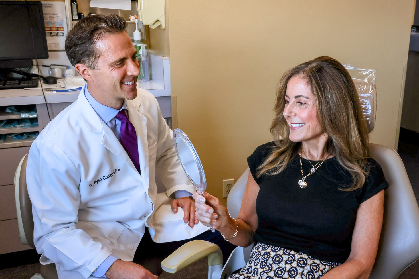 A patient checking her smile on a mirror while Dr. Conkle looks on