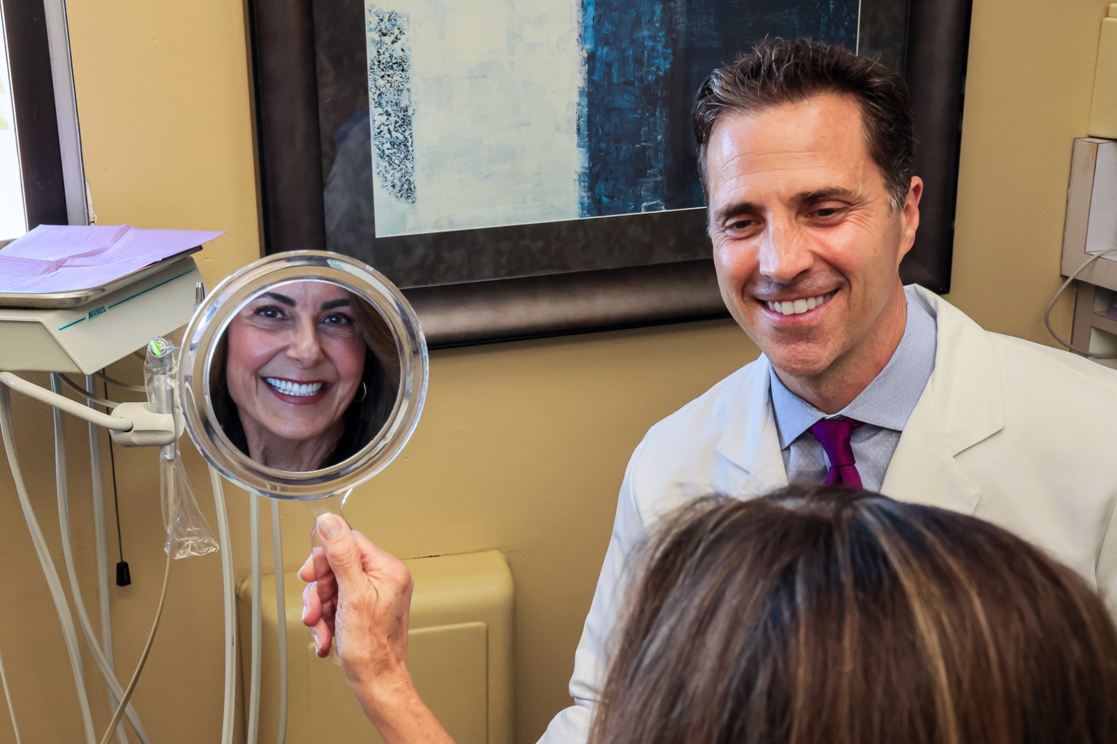 A patient checks her smile while Dr. Conkle looks on